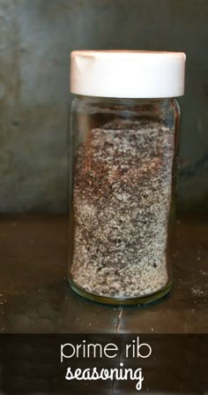 a glass jar filled with lots of different types of seasoning sitting on top of a table