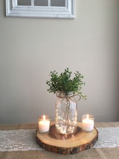 a table topped with candles and a vase filled with greenery on top of a wooden slice