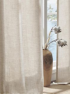 a vase with flowers in it sitting next to a window near the water's edge