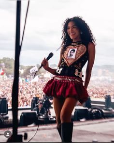 a woman in a short red skirt holding a microphone and standing on stage with an audience behind her