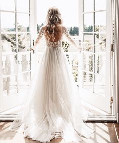 a woman is standing in front of an open door wearing a wedding dress with long sleeves