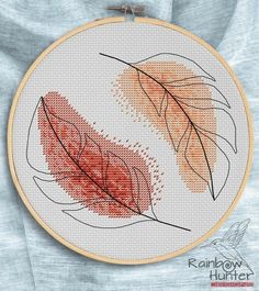 two orange and red leaves on a white background in a cross stitched hoop with the words rainbow hunt written across it