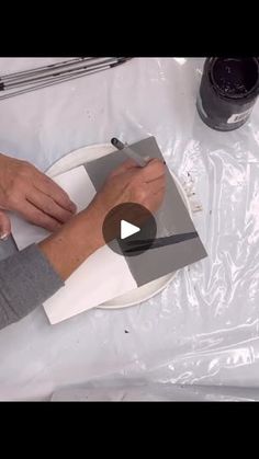 a person is cutting paper on top of a white surface with scissors and paint in the background