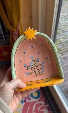 a hand holding a small bowl with flowers painted on the side and stars above it