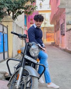 a man sitting on top of a motorcycle in the middle of an alleyway with buildings behind him