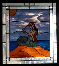 a stained glass window with a mermaid sitting on top of a rock in the ocean