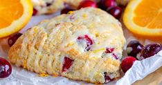 cranberry orange scones with icing sitting on wax paper next to sliced oranges