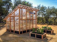 two small greenhouses with plants in them on the ground near some trees and grass