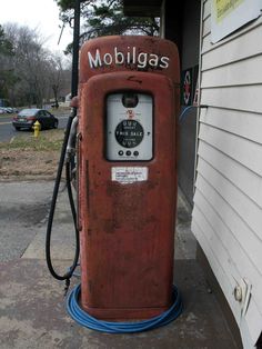 an old red gas pump sitting on the side of a building