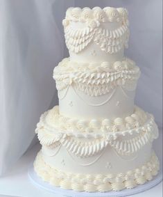 a three tiered white wedding cake with ruffles and pearls on the top