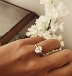 a person's hand with a diamond ring on it and flowers in the background