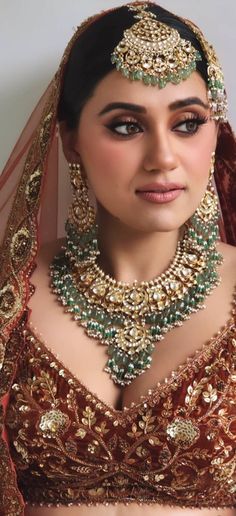 a woman in a red and gold bridal outfit with jewelry on her head,