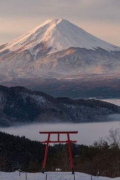 a snow covered mountain with a red bench in the foreground and fog on the ground