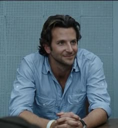 a man sitting at a table in front of a blue wall with his hands crossed