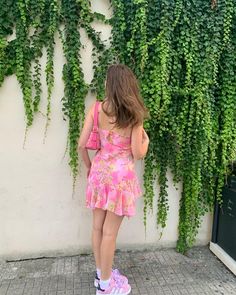 a woman in a pink dress standing next to a wall covered with green ivys