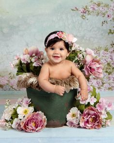 a baby sitting in a bucket with flowers on it's head and smiling at the camera