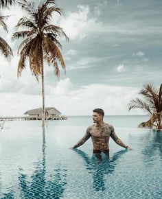 a man standing in the middle of a swimming pool with palm trees around his neck