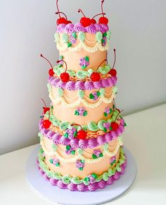 a three tiered cake with cherries on the top is decorated in pink, green and purple icing