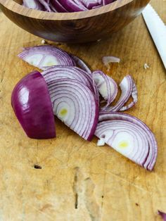 red onions are cut up in half on a cutting board next to a wooden bowl