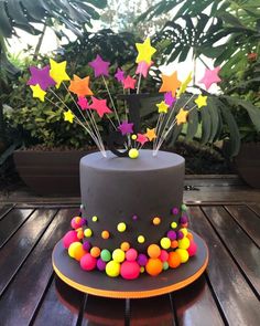 a cake decorated with stars and balloons on top of a wooden table next to potted plants