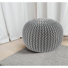 a gray and white knitted ottoman sitting on top of a rug next to a window