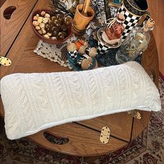 a wooden table topped with a white knitted pillow next to a bowl of food