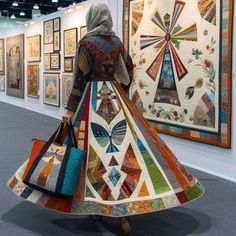 a woman in a colorful dress is looking at quilts on the wall behind her