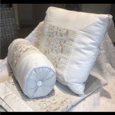 two pillows and a pillow on top of a white blanket with an embroidered flower design