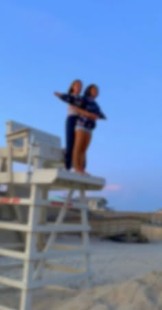 two people standing on top of a lifeguard tower with their arms around each other