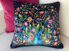 a decorative pillow on a white couch with colorful flowers and peacocks painted on it