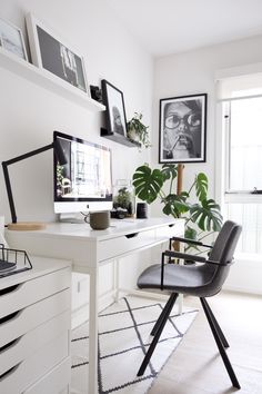 a white desk topped with a computer monitor next to a chair and potted plant