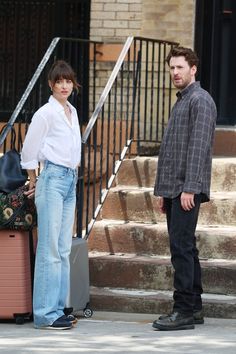 a man and woman standing on the street with their luggage in front of some stairs