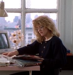 a woman sitting at a desk in front of a computer monitor with papers on it