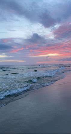 a beach with waves coming in to shore and the sun setting over the ocean behind it