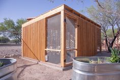 a small wooden structure sitting in the middle of a dirt field next to two metal buckets