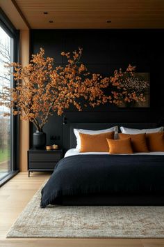 a bedroom with black walls and wooden flooring has a large bed that has orange pillows on it