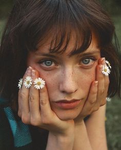 a woman with freckles on her fingers holding daisies in front of her face