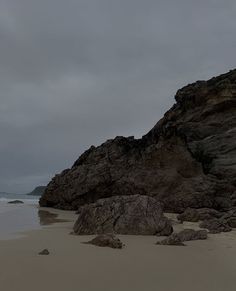 a large rock sitting on top of a sandy beach next to the ocean under a cloudy sky