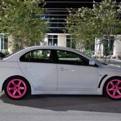 a white car with pink rims parked in front of a building