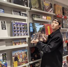 a man in a black coat is looking at cds on the wall and holding them with both hands