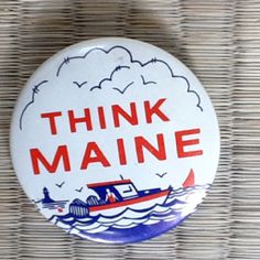 a button that says think maine with a boat in the water and clouds above it