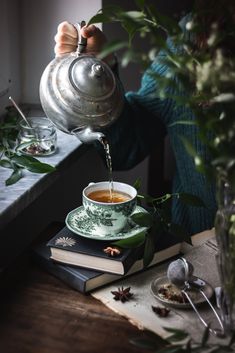 a person pouring tea into a cup on top of a table next to some books