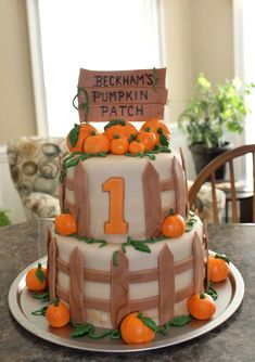 a three tiered cake decorated with pumpkins and a number one sign on top