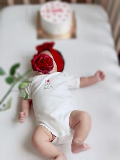 a baby laying on top of a bed next to a red rose and cupcake