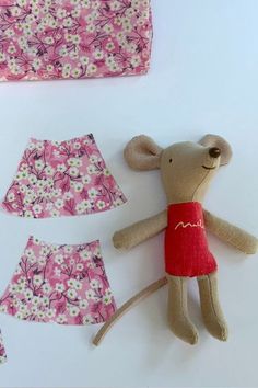 a teddy bear and two pieces of clothing laid out on a white surface with pink flowers in the background