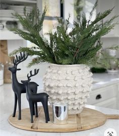 a white vase filled with green plants and two black deer figurines on top of a wooden tray