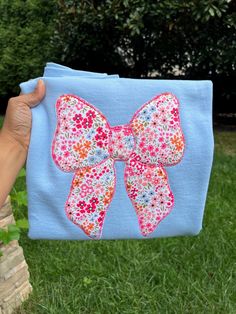 a person holding up a blue cloth with a pink flowered bow on the front