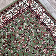 a green area rug with red and black designs on the bottom, along with a wooden floor