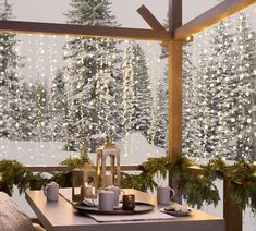 a table set for two with candles and christmas decorations on it in front of a snowy forest