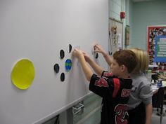 a young boy writing on a white board with magnets attached to the back of it